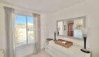 Helles Schlafzimmer mit weißer Kommode, Spiegel und Fenster mit Blick auf Palmanova
