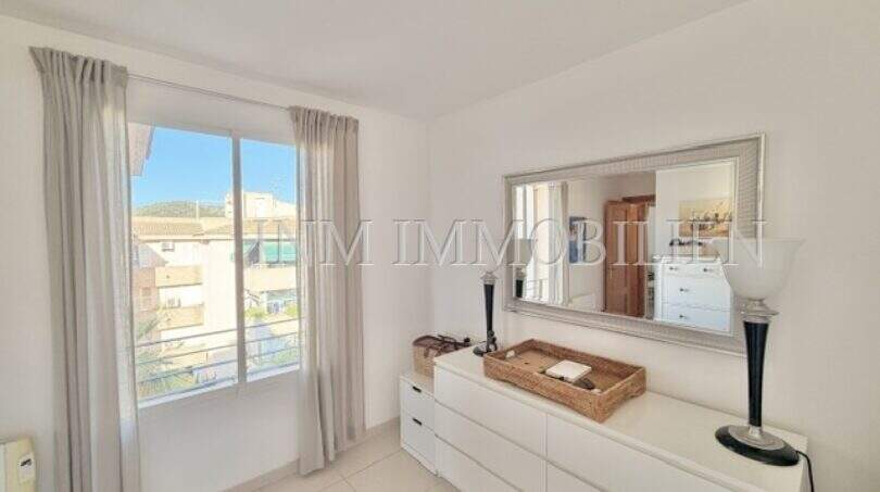 Helles Schlafzimmer mit weißer Kommode, Spiegel und Fenster mit Blick auf Palmanova