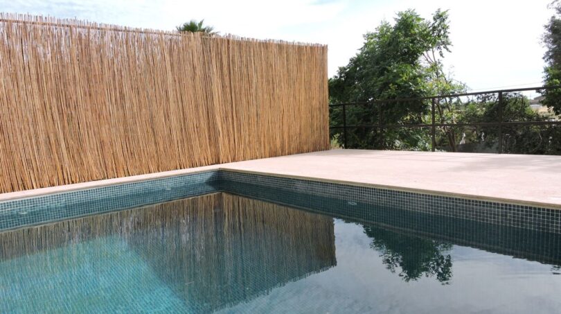 Pool der Finca in Manacor mit Mosaikfliesen, hellem Steinbelag und Sichtschutz aus Bambus