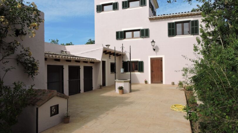 Außenansicht der Finca in Manacor mit weißer Fassade, grünen Fensterläden und gepflastertem Innenhof