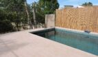 Pool der Finca in Manacor mit hellem Fliesenrand, Schilfmatte als Sichtschutz und üppigem Baumbestand