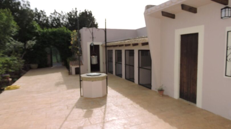 Sonniger Innenhof der Finca Manacor mit Steinboden, dekorativem Brunnen und weißen Gebäuden mit Holzbalken.