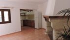 Wohnbereich der Finca Manacor mit rustikalem Kamin, Terrakottaboden und offener Küche mit Holzbalken