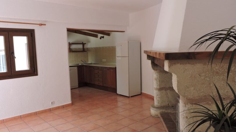Wohnbereich der Finca Manacor mit rustikalem Kamin, Terrakottaboden und offener Küche mit Holzbalken