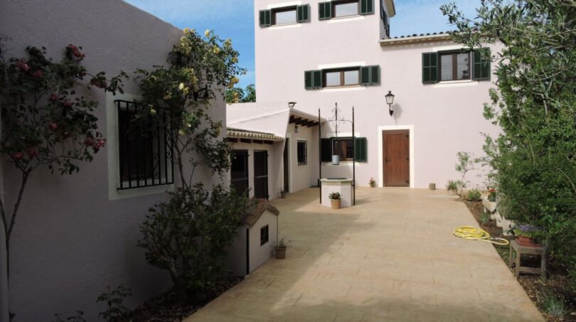 Außenansicht der Finca Manacor: weißes Herrenhaus mit grünen Fensterläden, gepflastertem Innenhof und üppigem Bewuchs