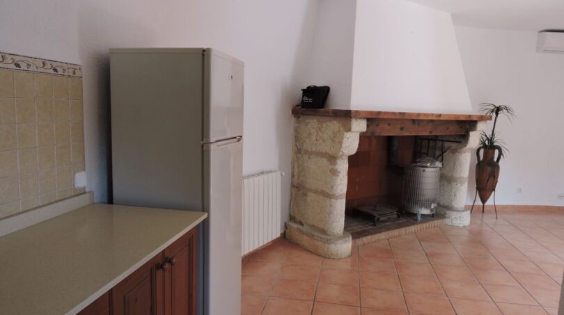 Küche der Finca Manacor mit Kühlschrank, Holztheke und rustikalem Steinkamin mit Holzbalken