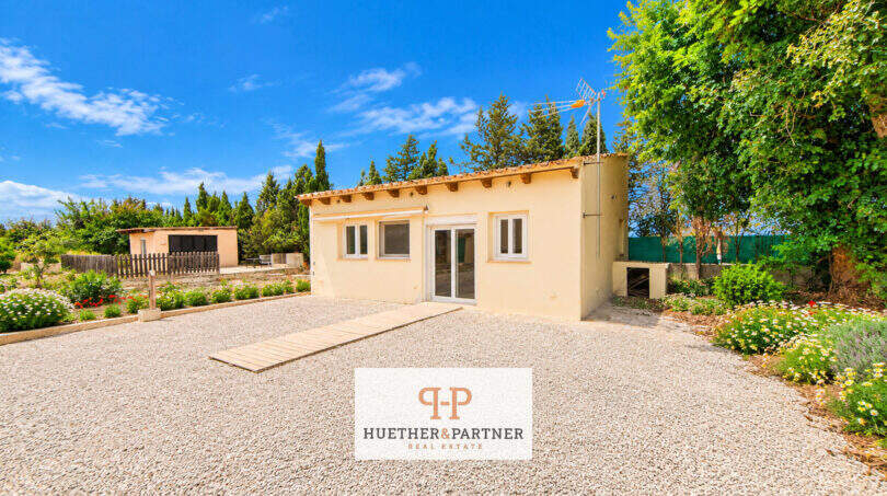 Außenansicht der Finca Santa Maria: kleines Gästehaus mit Kiesfläche, Garten und Bäumen nahe Palma