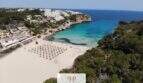 Luftaufnahme der Bucht Cala Mandia in Porto Cristo Novo mit türkisblauem Wasser, Sandstrand und Villen in Strandnähe.