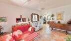 Helles Wohnzimmer der Finca mit rotem Sofa, Terrakottaboden, Deckenventilator und Rundbogen-Durchgang.