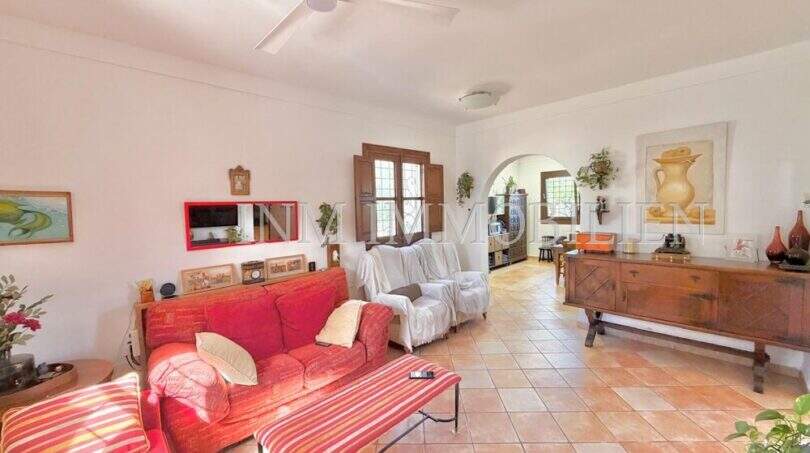 Helles Wohnzimmer der Finca mit rotem Sofa, Terrakottaboden, Deckenventilator und Rundbogen-Durchgang.