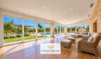Lichtdurchflutetes Wohnzimmer der Finca Santa Maria mit Panoramafenstern, Holzboden und Blick auf Pool und Garten.