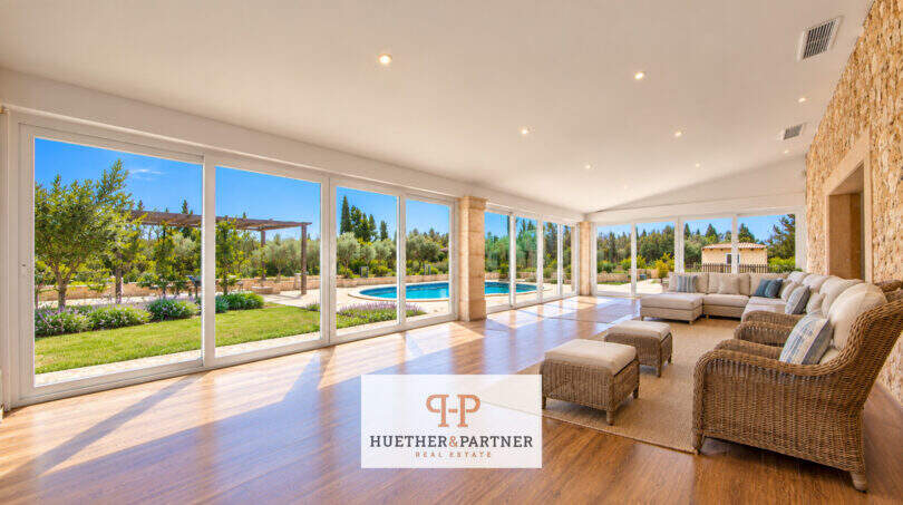 Lichtdurchflutetes Wohnzimmer der Finca Santa Maria mit Panoramafenstern, Holzboden und Blick auf Pool und Garten.