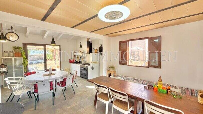 Helles Esszimmer mit Holzdecke, zwei Esstischen und offener Küche der mediterranen Finca bei Algaida