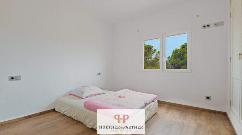 Helles Schlafzimmer der Finca Santa Maria mit Holzboden, Doppelbett und Blick auf grüne Bäume.
