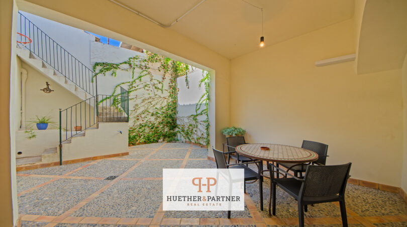Überdachte Terrasse mit Esstisch, Steinfliesen und begrüntem Innenhof mit Treppe in Stadthaus Manacor