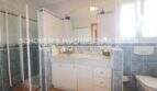 Badezimmer mit Glasdusche, weißem Waschtischunterschrank, Spiegel und WC, blaue Fliesenwände, Sa Coma