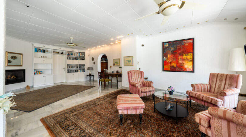 Helles Wohnzimmer der Villa in Cala Murada mit Kamin, Bücherregal, Orientteppich und rosa Sesseln.