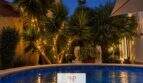 Beleuchteter Pool bei Nacht mit Palmen und Steinlöwen-Skulpturen, Haus in Cala Murada