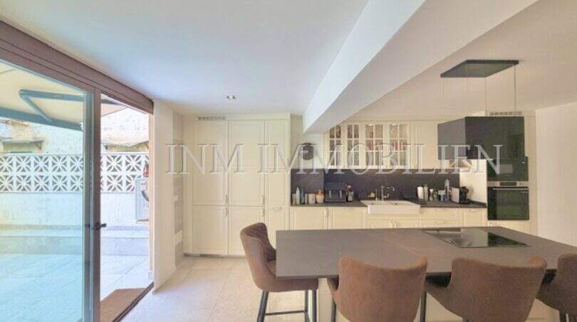 Moderne Küche mit Kochinsel, cremefarbenen Schränken und Zugang zur Terrasse in sanierter Wohnung in Pere Garau