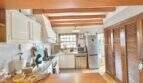 Cocina rústica con techo de vigas de madera, armarios blancos y refrigerador de acero inoxidable en casa mediterránea Sa Ràpita
