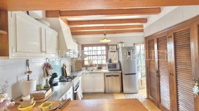 Cocina rústica con techo de vigas de madera, armarios blancos y refrigerador de acero inoxidable en casa mediterránea Sa Ràpita