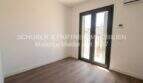 Dormitorio claro con suelo de madera, aire acondicionado y acceso al balcón en apartamento esquinero de nueva construcción en Cala Millor