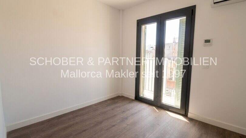 Dormitorio claro con suelo de madera, aire acondicionado y acceso al balcón en apartamento esquinero de nueva construcción en Cala Millor