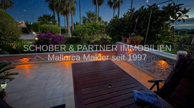 Terraza vespertina iluminada con mesa de madera, palmeras y cielo estrellado del apartamento de 4 habitaciones en Cala Millor