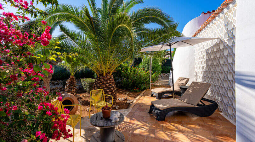 Sunny terrace of the sea view villa in Cala Murada with sun loungers, palm tree and bougainvillea flowers