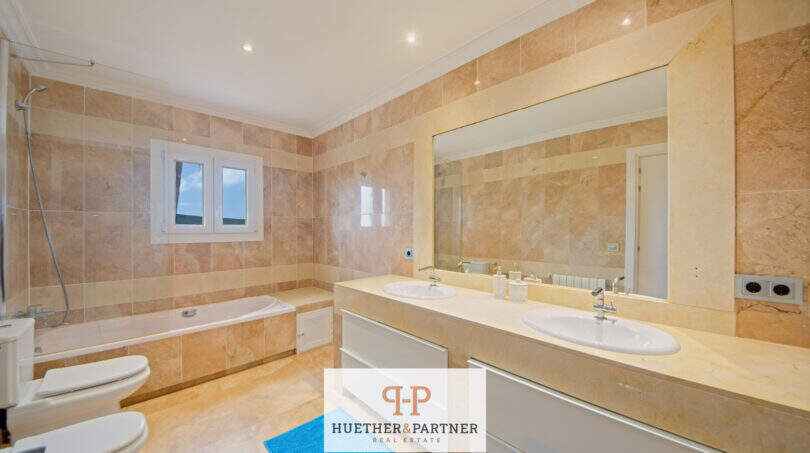 Helles Badezimmer der Finca Santa Maria mit Doppelwaschbecken, Badewanne und Marmorfliesen in Beige.