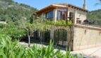 Außenansicht Landhaus Llucmajor: Mediterrane Finca mit Glasfassade, Holzelementen, Terrasse und Bergblick.