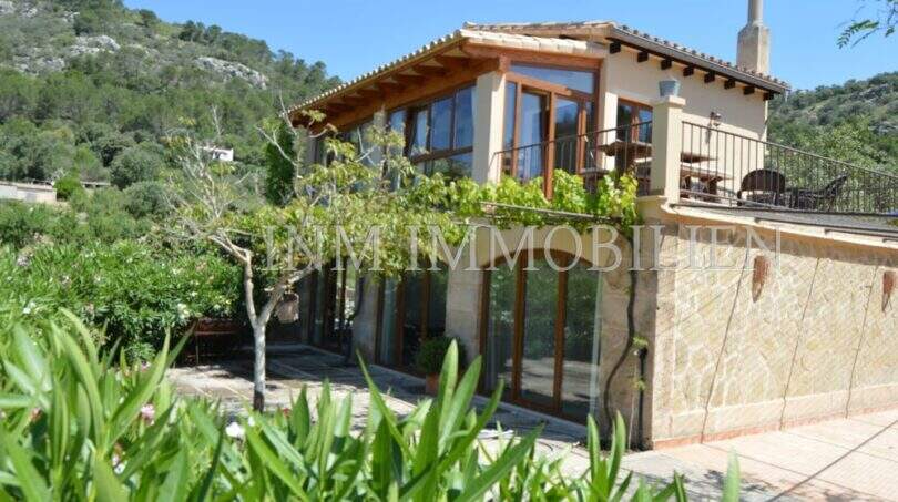 Außenansicht Landhaus Llucmajor: Mediterrane Finca mit Glasfassade, Holzelementen, Terrasse und Bergblick.