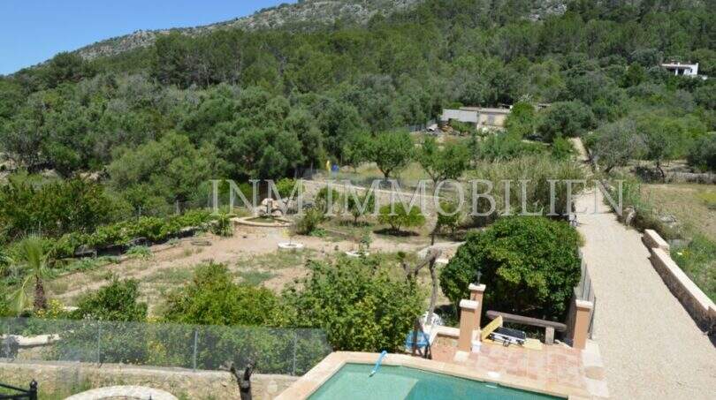 Außenbereich des Landhauses in Llucmajor mit Pool, gepflegtem Garten und Blick auf bewaldete Hügel.