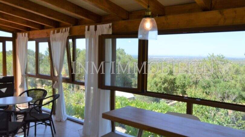 Veranda mit Holzbalkendecke, weißen Vorhängen und Panoramablick über Llucmajors Landschaft bis zum Meer.