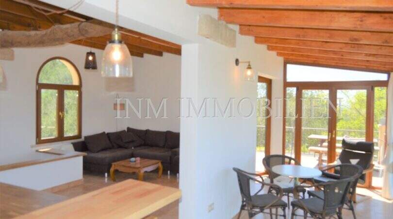 Offener Wohn-Essbereich mit Holzbalkendecke, dunklem Sofa und Terrassenzugang im Landhaus Llucmajor