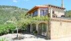 Außenansicht Landhaus Llucmajor: Mediterrane Fassade mit Holzfenstern, Balkon, Terrasse und Bergkulisse.