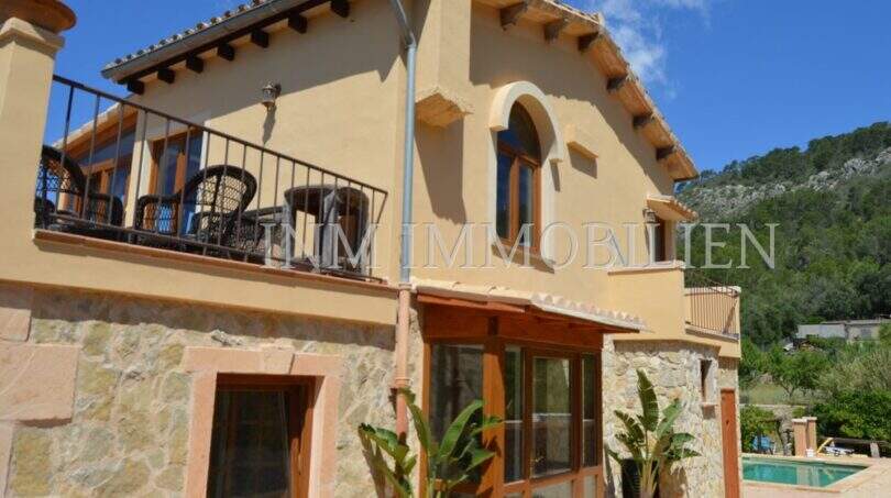 Außenansicht Landhaus Llucmajor: Mediterrane Villa mit Balkon, Natursteinwand und Pool im Hintergrund.
