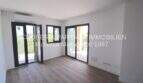 Sala de estar luminosa con suelo de madera, dos puertas balconeras y aire acondicionado en apartamento esquinero de nueva construcción en Cala Millor.