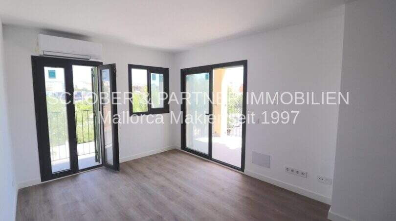 Sala de estar luminosa con suelo de madera, dos puertas balconeras y aire acondicionado en apartamento esquinero de nueva construcción en Cala Millor.