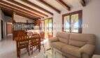 Living room with wooden beam ceiling, leather sofa and open kitchen of the finca in Son Carrió, Mallorca.