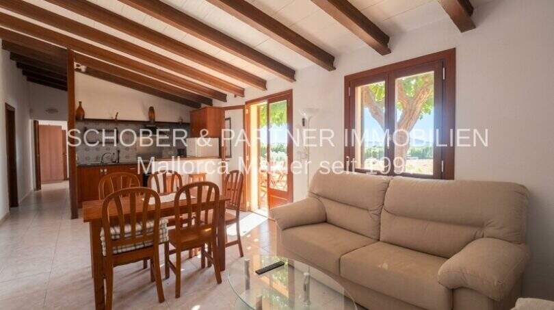 Living room with wooden beam ceiling, leather sofa and open kitchen of the finca in Son Carrió, Mallorca.