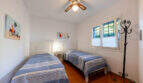 Bright bedroom of the villa in Cala Murada with two single beds, terracotta floor and ceiling fan.