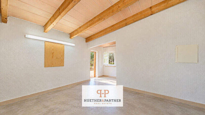 Leerer Raum der Finca Santa María mit Holzbalkendecke, Betonboden und Durchgang zum Außenbereich.