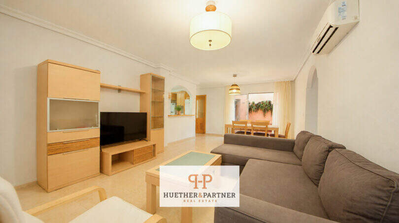 Helles Wohnzimmer der Erdgeschosswohnung Cala Antena mit Sofa, TV-Einheit und Essbereich