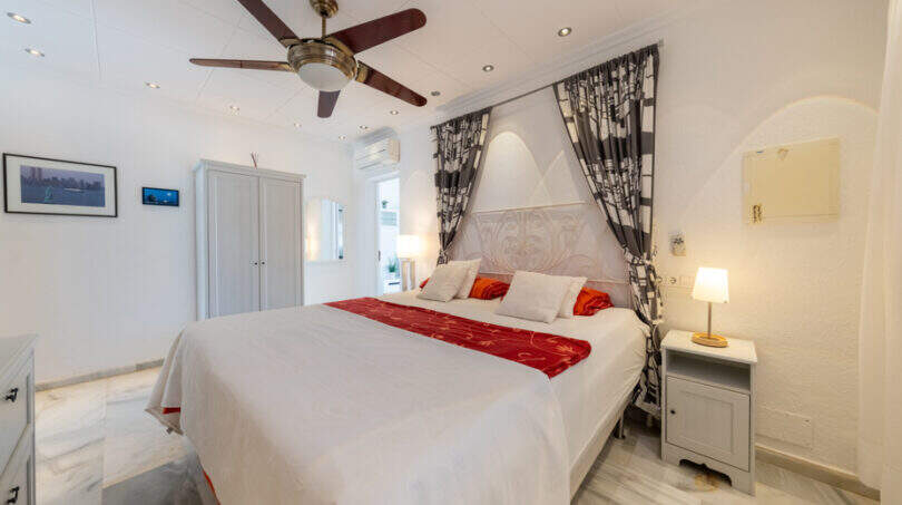 Helles Schlafzimmer der Poolvilla in Cala Murada mit Doppelbett, Deckenventilator und elegantem weißen Ambiente.