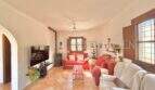 Helles Wohnzimmer der Finca bei Algaida mit Terrakottaboden, roten Sofas, Kaminofen und Deckenventilator.