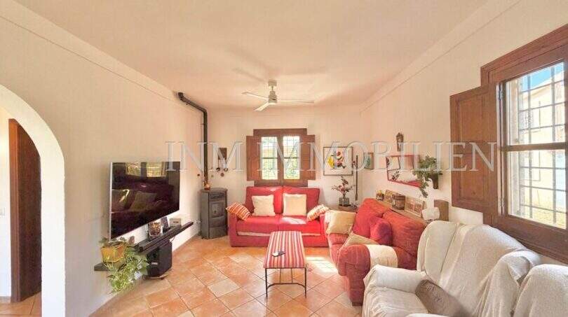Helles Wohnzimmer der Finca bei Algaida mit Terrakottaboden, roten Sofas, Kaminofen und Deckenventilator.