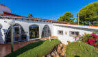 Exterior view of the sea view villa in Cala Murada with white facade, tile roof, wrought iron grilles and well-maintained garden.