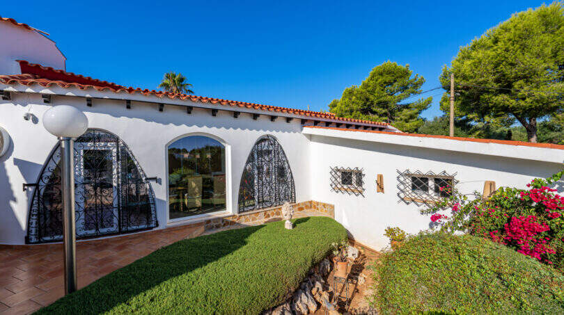Exterior view of the sea view villa in Cala Murada with white facade, tile roof, wrought iron grilles and well-maintained garden.
