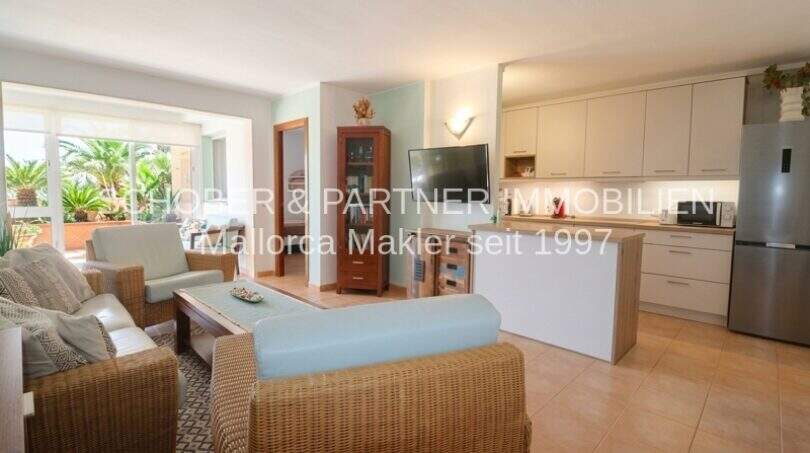 Helles Wohn-Esszimmer mit Rattanmöbeln, offener Küche und Zugang zur Terrasse in Sa Coma